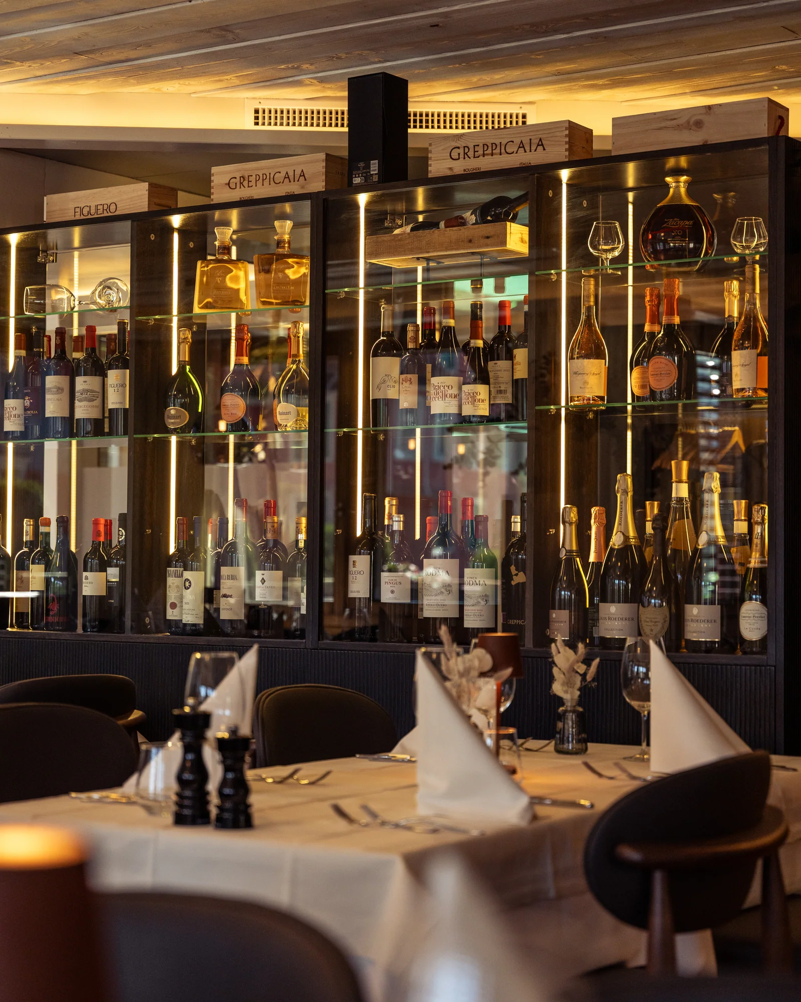 Gedeckte Tische vor dem beleuchteten Weinschrank im Restaurant-Pizzeria Wies